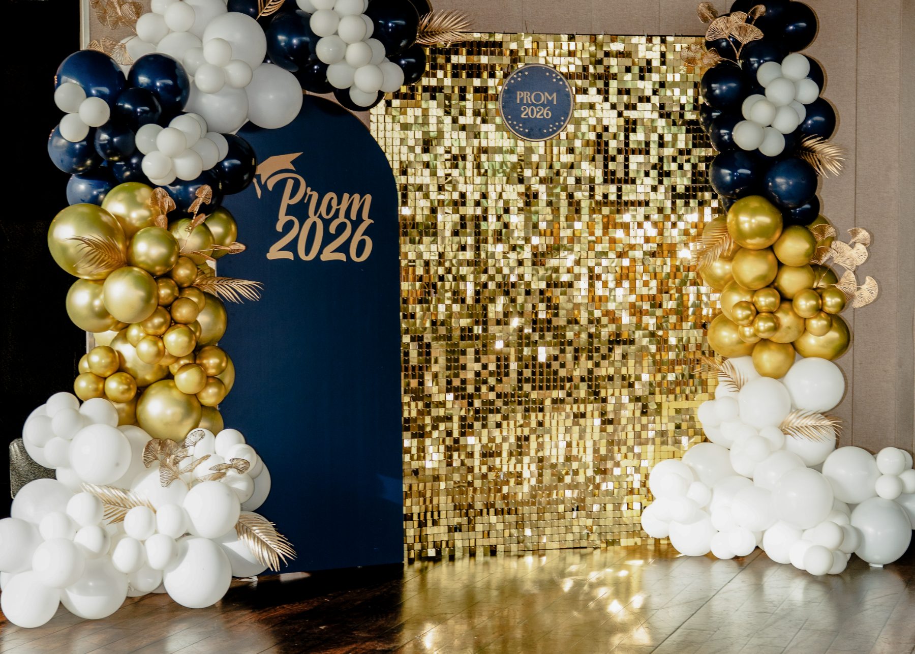 Elegant event backdrop with a gold sequin wall, navy arch and gold and white balloon garlands