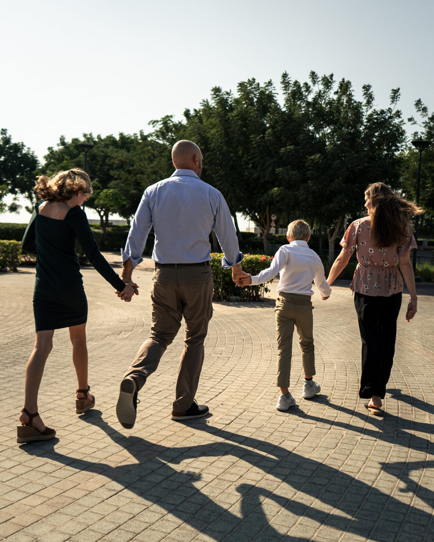 A family of four walking hand in hand through a sunlit Dubai park at golden hour