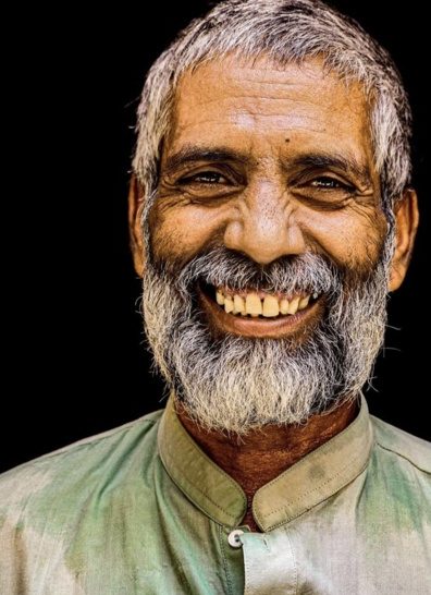 Editorial portrait of a smiling elderly man with a grey beard against a black background