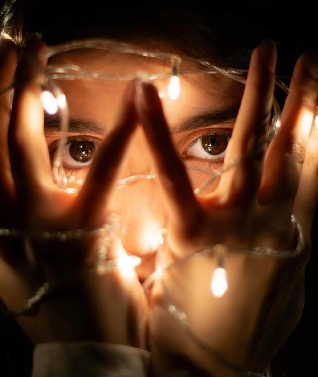 Cinematic close-up of a face lit by warm fairy lights held in cupped hands